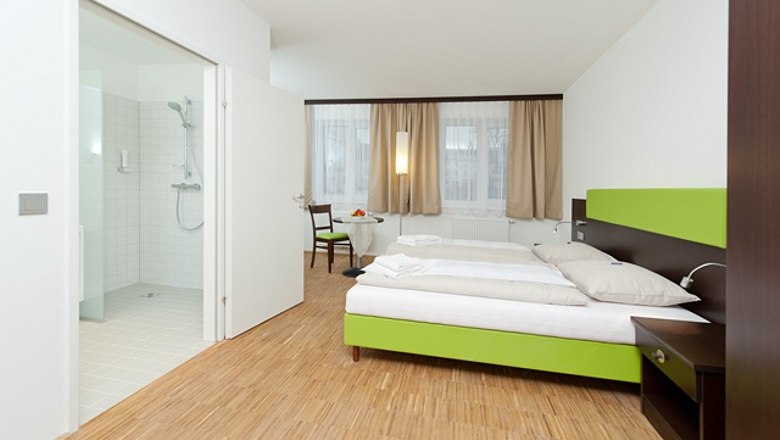 Modern hotel room with double bed, wooden floor and adjoining bathroom.