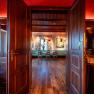 View through open wooden doors into a cozy room with wooden floor, table and chairs, decorated with lamps and curtains.