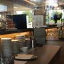 Breakfast counter with stacked plates, cutlery and pastries under a glass bell jar.