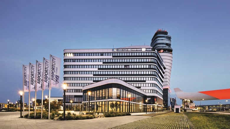 Modern building at Vienna Airport at dusk with flags and control tower in the background.