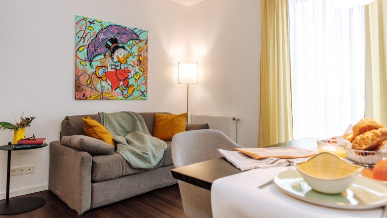 Living room with gray sofa, colorful comic art on the wall, yellow curtains and breakfast table.