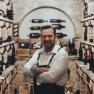 A man in a wine cellar with shelves full of wine bottles.