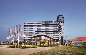 Modern building at Vienna Airport at dusk with flags and control tower in the background.