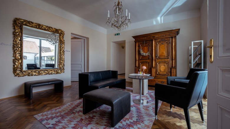 Elegant living room with antique wardrobe, large mirror, black leather furniture and a chandelier.