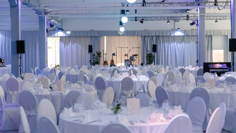 Elegant function room with round tables set in white and a stage with musical instruments.