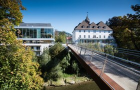Modern and historic building with bridge in green surroundings.