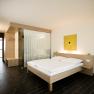 Modern hotel room with double bed, wooden furniture and yellow artwork on the wall.