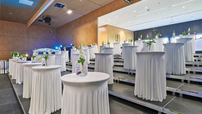 An event room with high bar tables covered in white, decorated with flowers and information material.