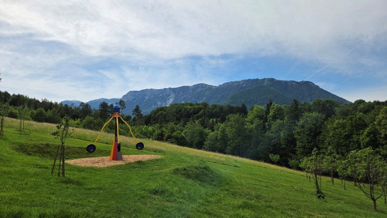 A children's playground with a seesaw set against a mountain landscape, with the Rax in the background.