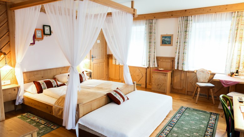 Cozy hotel room with four-poster bed, wooden furniture and carpets.