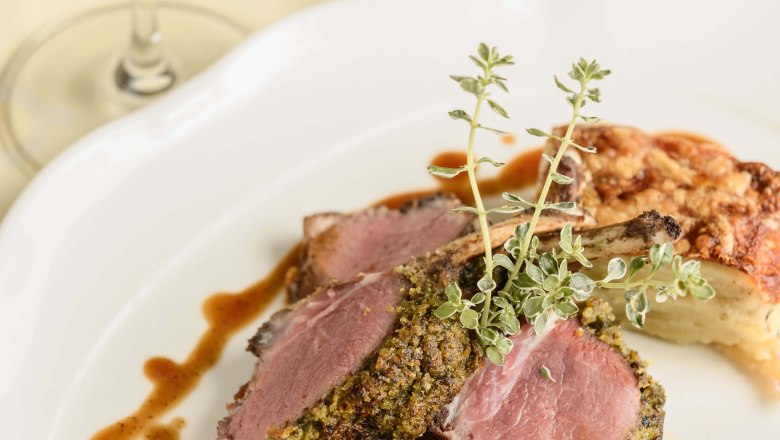 A plate with herb-crusted lamb chops, vegetable garnish and sauce, with a glass of red wine next to it.