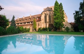 Historic building with pool in the foreground, surrounded by trees and garden.