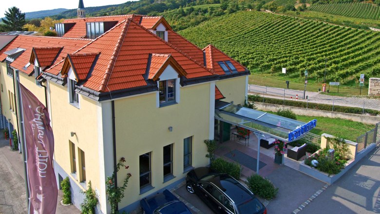 Exterior view of the Hotel Turmhof with red roofs and surrounding vineyards.