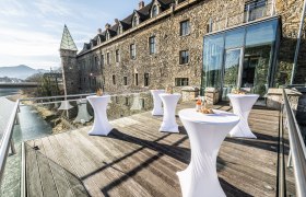 Terrace with bar tables in front of a historic building with a glass façade.