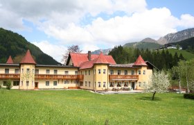 A large hotel with red roofs in a green, mountainous landscape.