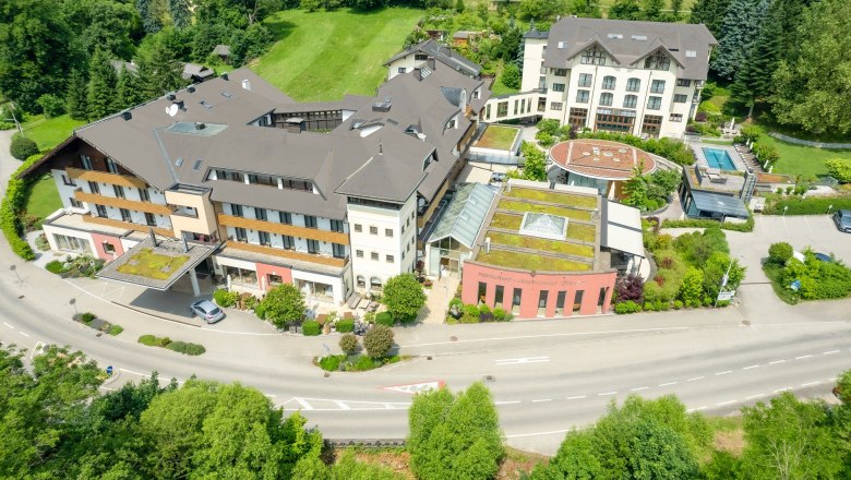 Aerial view of a large hotel complex with several buildings, surrounded by green landscape.
