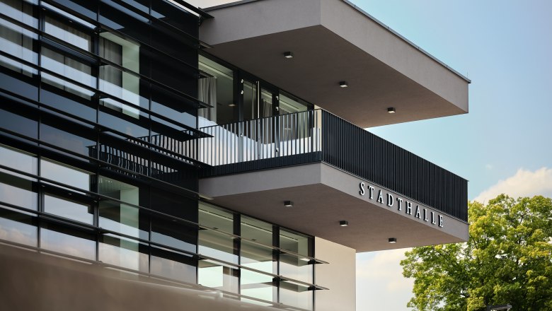 Modern exterior view of the Stadthalle Ybbs with glass façade and balcony.