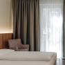 Modern hotel room with bed, armchair and curtains.