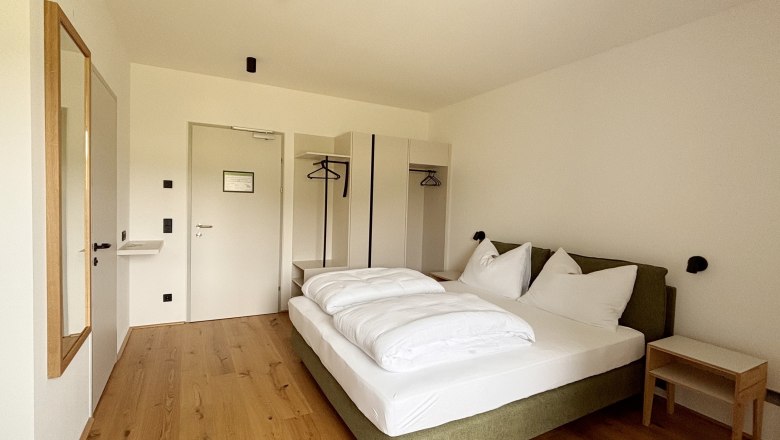 A modern double room with a large bed, wooden floor, closet and a mirror on the wall.