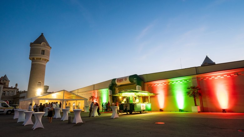 Outdoor evening event with illuminated building and tents.