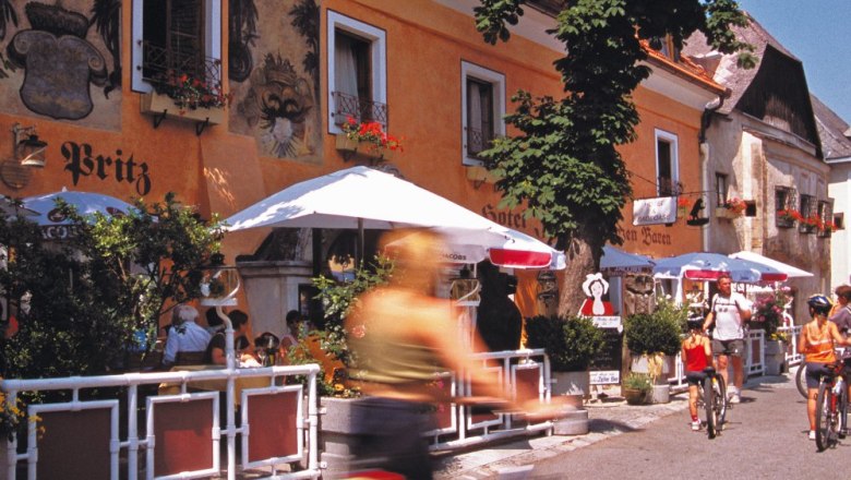 Cyclists in front of a hotel with a terrace and parasols.