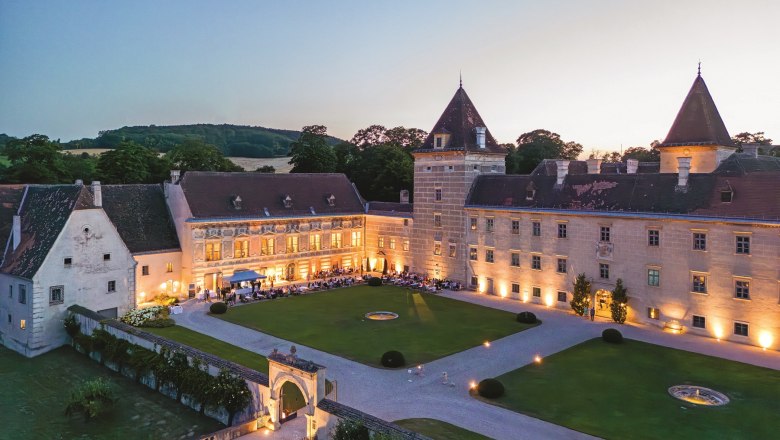 Aerial view of Walpersdorf Castle at dusk, illuminated with guests at a garden party in the courtyard.