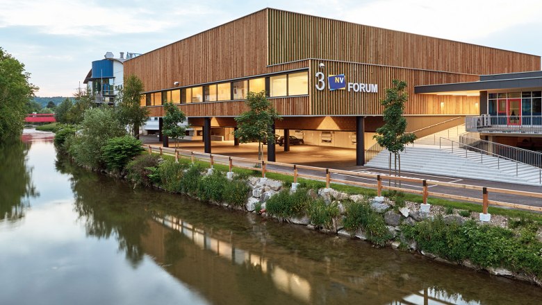 Modern Messe Wieselburg building with wooden fa&ccedil;ade and river in the foreground.