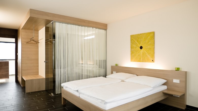 Modern hotel room with double bed, wooden furniture and yellow artwork on the wall.