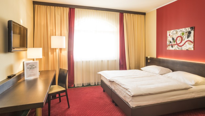 A cozy hotel room with a double bed, red carpet, desk, TV and modern art on the wall.