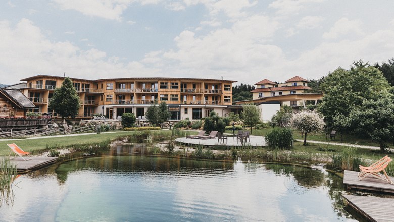 Hotel building with natural pond and sun loungers in the foreground.