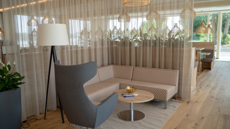 Modern seating area with gray armchair, patterned sofa, round wooden table and floor lamp in front of a curtain.