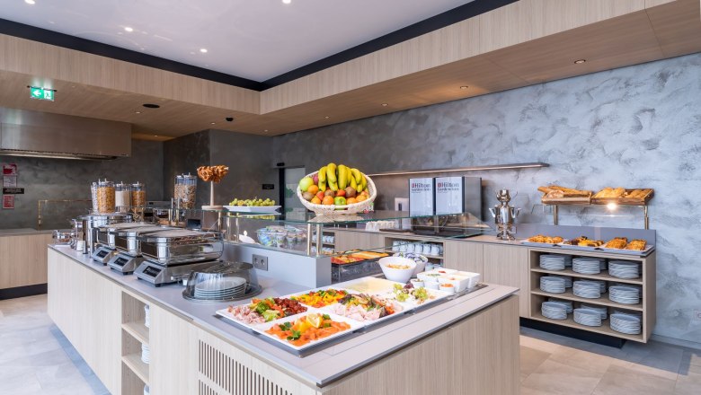 A rich breakfast buffet with fruit, pastries, cold cuts and cereals in a modern hotel restaurant.