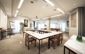Conference room with U-shaped tables and chairs, flipchart and plants.