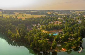 Aerial view of a lake with surrounding forest and buildings.