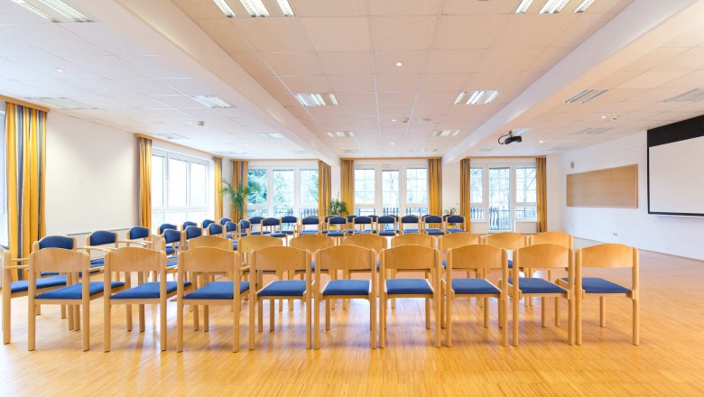 A bright seminar room with rows of chairs, large windows, and a projector mounted on the ceiling.