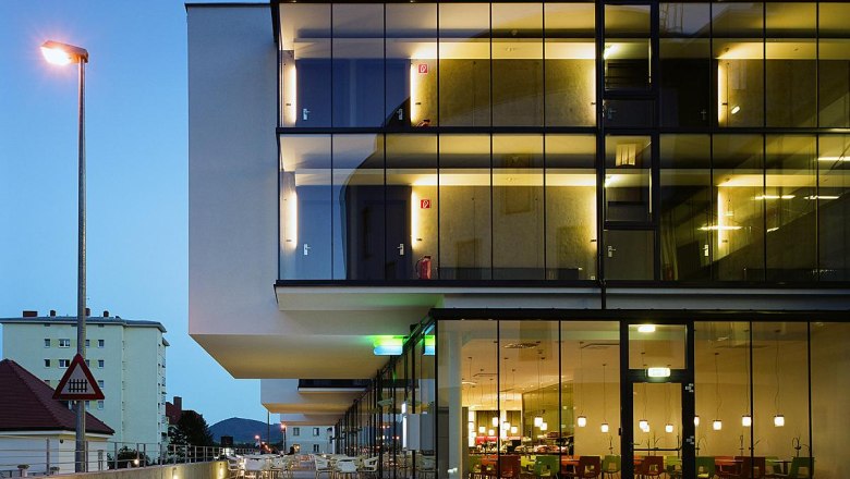 Modern hotel building with glass fa&ccedil;ade at dusk, illuminated interiors visible.