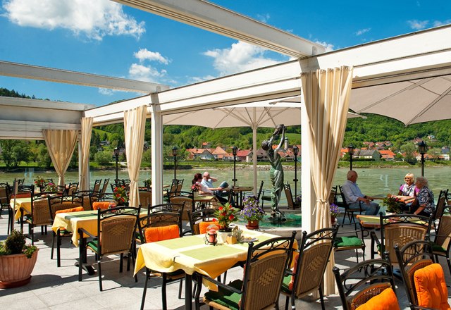 Restaurant terrace with a view of a river and green hills in the background.